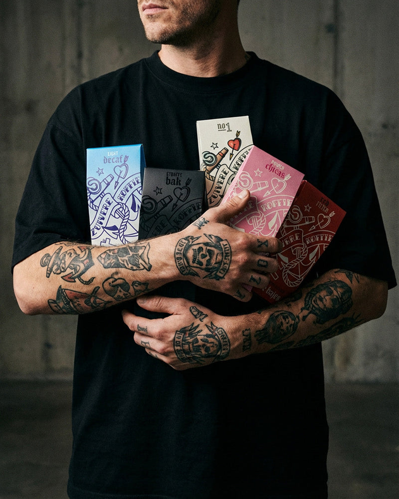 Man met tatoeages heeft alle Zuivere Koffie producten vast.